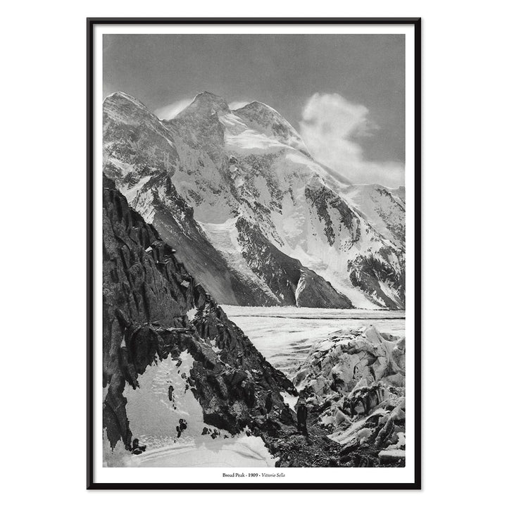 Black and white photograph and poster of Broad Peak by Vittorio Sella showing snow covered mountains and mountaineers climbing amidst rocky terrain and glacier, with black aluminium frame on white background