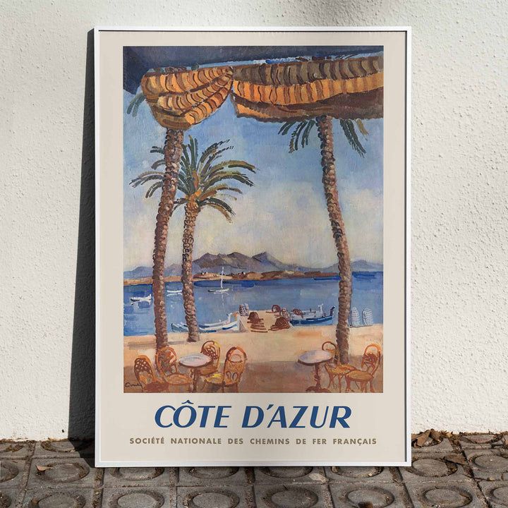 Edmond Céria French Riviera Railway poster with palm trees, blue sea, sandy beach, ochre canopies, vintage travel style, framed and displayed in home decor