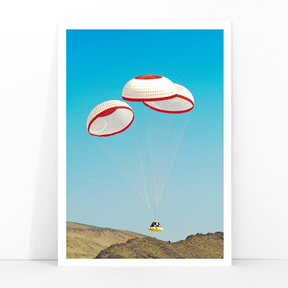 CST-100 crew capsule landing with three parachutes over desert landscape by NASA and The Boeing Company poster artwork, framed and displayed in modern living room decor