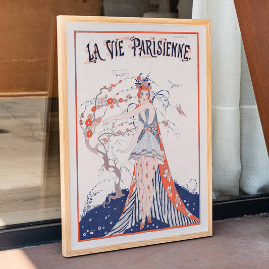Elegant Art Deco poster of a woman in a floral dress standing by a blossoming tree La Vie Parisienne by Umberto Brunelleschi, framed and displayed in home decor