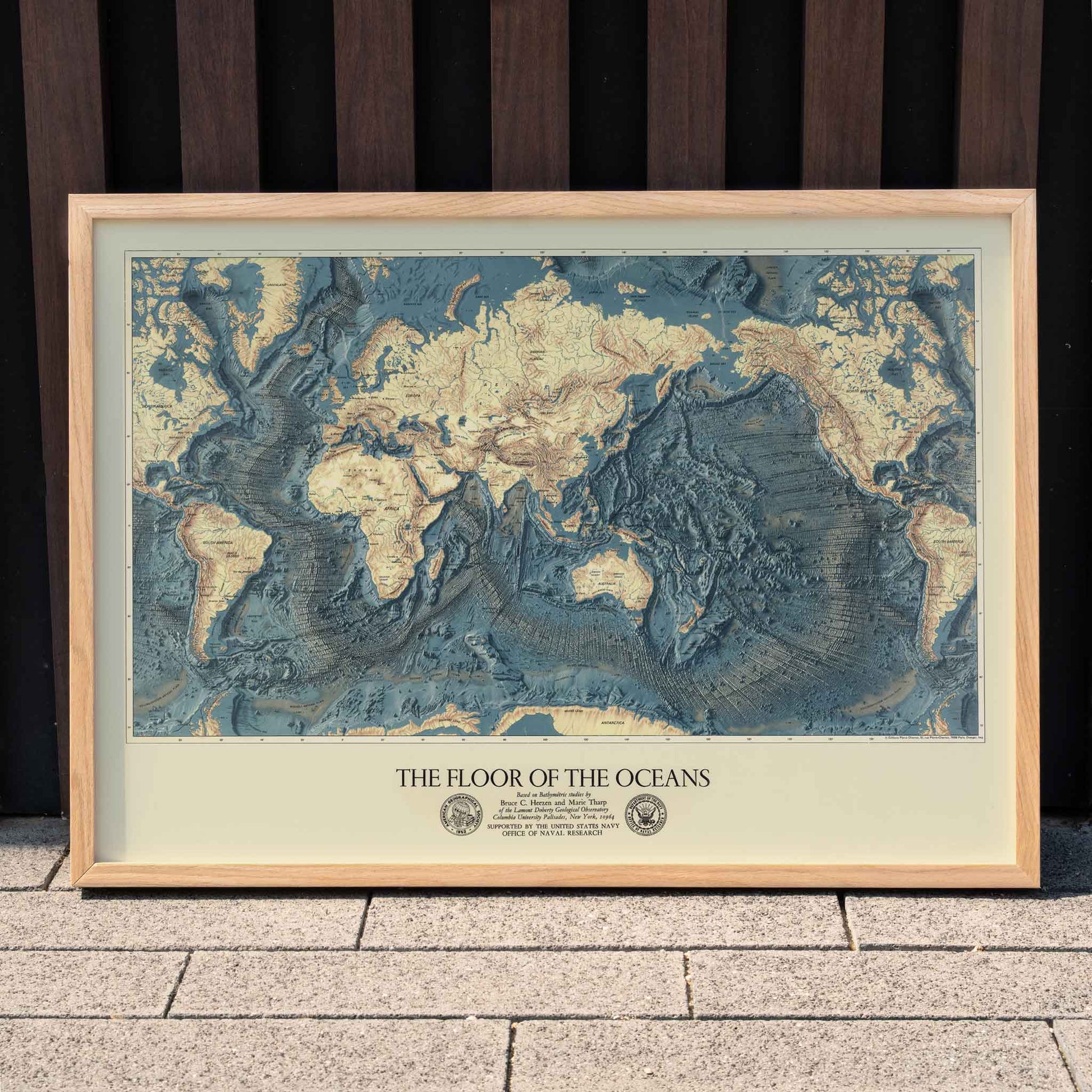 World map artwork showing ocean floors titled The Floor of the Oceans bathymetric map poster, framed and displayed in home decor
