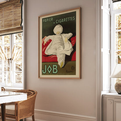 Cigarette Rolling Paper Job poster by Leonetto Cappiello showing a relaxed man in white robes and turban reclining with a cigarette on a red couch, framed and displayed in home decor