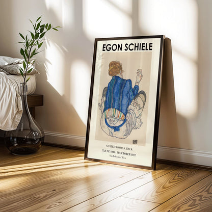 Egon Schiele Woman Seated Back exhibition poster showing a woman in a colorful garment sitting with her back turned artwork, framed and displayed in modern living room decor